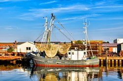 Ein Fischkutter bei Sonnenschein und blauem Himmel im Hafen in Dithmarschen 
