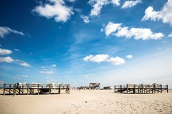 Stelzenhäuser am Strand von St. Peter-Ording bei blauem Himmel und Sonne